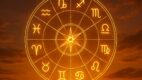 Zlatni horoskopski točak sa zodijačkim simbolima svetli na nebu obasjanom zalaskom sunca i oblačnim horizontom.