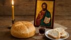 Slavska trpeza sa hlebom, svećom, ikonom Svetog Jovana i čašom vina na drvenom stolu.