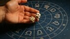 Ruka baca kockice preko astrološke karte sa horoskopskim znacima.