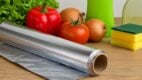 Rolna aluminijumske folije na kuhinjskom pultu, okružena svežim povrćem i sredstvima za čišćenje