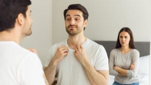 Muškarac se gleda u ogledalo, žena nezadovoljna u pozadini.