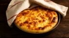 Pita sa zlatno-pečenom korom delimično prekrivena krpom, u plehu na drvenoj površini.