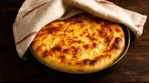 Pita sa zlatno-pečenom korom delimično prekrivena krpom, u plehu na drvenoj površini, prazna pita