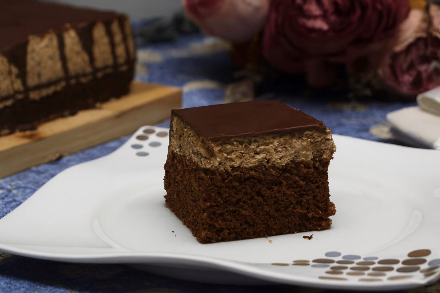 Posna poslastica sa tri sloja na dekorativnom tanjiru, u pozadini cela torta i suvo cveće